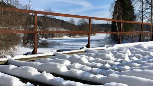 Bron i vinterskrud. Sliten gammal snöbeklädd järnvägsbro i trä över ett vattendrag en vinterdag.