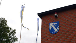Mörskom vill hjälpa alla sina företagare, men speciellt dem som har det svårt på grund av pandemin. En husvägg med en vapensköld i blått synns mot en grå himmel. Bredvid vajar några vimplar med samma vapen, ett vitt träd mot blå botten.