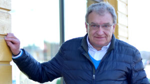 Roger Hafström (Saml) anser att skolnätet ska bevaras i sin nuvarande form. Det ska sparas på andra håll än inom bildningen. En man står och lutar handen mot en vägg med fönster. Han tittar in i kameran.