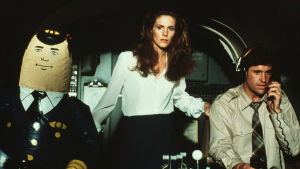 Elaine Dickinson (Julie Hagerty) och Ted Striker (Robert Hays) spelade huvudrollerna i Airplane! Bredvid dem autopiloten. Elaine Dickinson (Julie Hagerty) och Ted Striker (Robert Hays) i cockpiten tillsammans med en så kallad uppblåsbar autopilot.