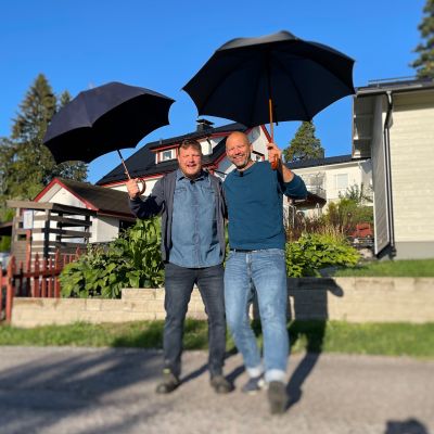 Två personer står i solskenet med paraplyn.