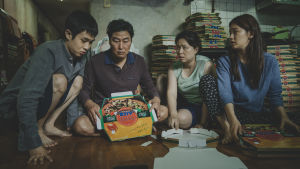 Familjen Kim med sonen Ki-woo (Woo-sik Choi), pappa Ki-taek (Song Kang-ho), mamma Chung-sook (Hye Jin Jang) och dottern Ki-jung (So-dam Park). Familjen Kim sitter på golvet i sin källarlägenhet och viker ihop pizzakartonger.