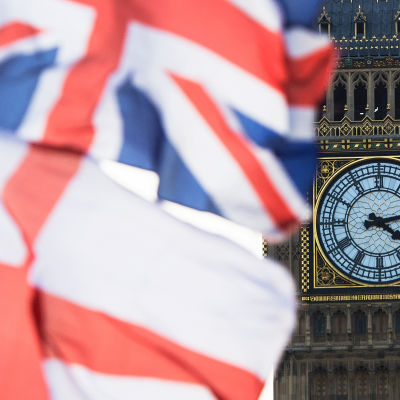 Brittiska och engelska flaggan fladdrar i vinden framför Big Bens urtavla vid brittiska parlamentet.