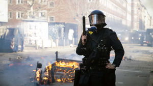 Demonstration på Blågårds Plads på Nørrebro i Köpenhamn ledde till stenkastning och att bilar stacks i brand. Högernationalisten Rasmus Paludans provocerande demonstrationer har fått mycket kritik i Danmark under våren, och har lett till våldsamma sammandrabbningar mellan motdemonstranter och polisen. Polis med hjälm och gasmask håller ett vapen i handen och på gatan brinner något.