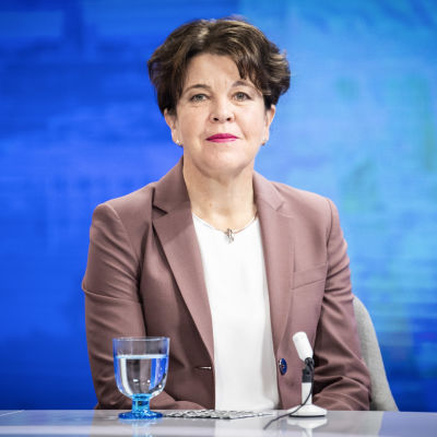 Mörkhårig kostymklädd sittande kvinna mot en blå bakgrund. Chefen för Europeiska kompetenscentret för motverkande av hybridhot Teija Tiilikainen i Yles studio i september 2020.