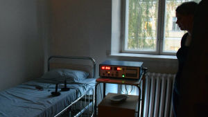 Från ljudinstallationen på Lappvikens mentalsjukhus. Personer står i mörkt rum intill sjukhussäng och elbehandlingsapparat.