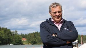 Mikael Pentikäinen fick en välkomstgåva av Företagarna i Ingå: En mörkblå luvtröja. Mikael Pentikäinen står iklädd en mörkblå luvtröja vid vattnet.