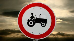 Om man kör traktor är man nog en man, antar skylten ... Skylt av en bonde som kör traktor. Mörka moln i bakgrunden.