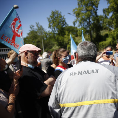 Personer står med ryggen mot kameran. De står utanför en Renaultfabrik i Frankike. På en persons jacka står det Renault.