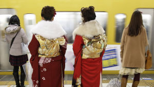 Kaksi kimonopukuista naista odottavat metrojunaa asemalaiturilla.