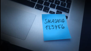 Tässä on malliesimerkki huonosta salasanasta. Käsitelty kuva läppäristä, johon liimattu sininen post-it lappu. Lapussa teksti salasana 123456