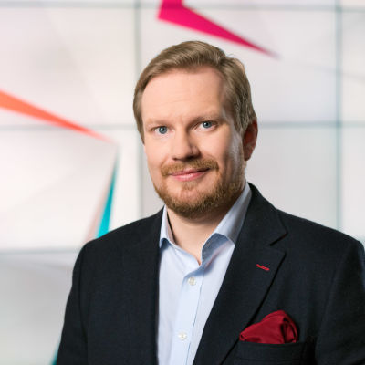 Programledare Ted Urho poserar framför Yles nyhetsgrafik.