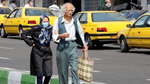 Många iranier ignorerar hotet från coronaviruset medan försöker skydda sig en äldre man och en kvinna iförd ansiktsmask promenerar längs en gata i Teheran