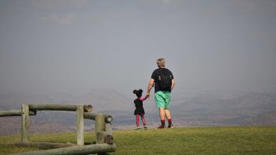 En liten flicka med sin pappa står med ryggarna mot kameran. De står på kanten av en kulle och ser över ett stort öde landskap.