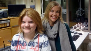 Hanna Grandell och Ann-Sofie Nyholm. Hanna Gardell och Ann-Sofie Nyholm står vid ett skrivbord. I bakgrunden syns en tv och en adventsljusstake.