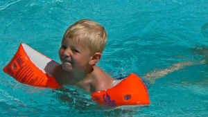 Det finns olika sätt att lära barn simma. En pojke som simmar i en pool med armpuffar på sig.