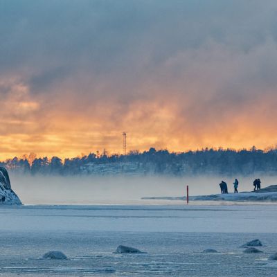 Ihmiset ihailevat merisumua ja auringonlaskua Helsingissä meren äärellä.