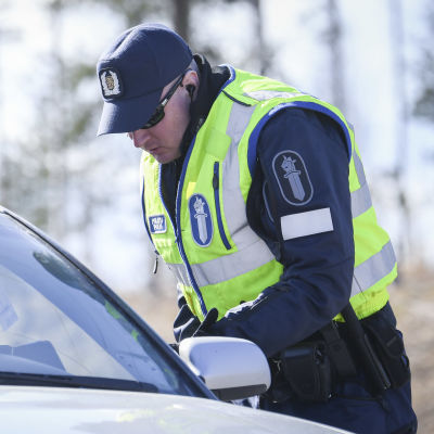 En polis kontrollerar körkortsuppgifter hos en person i en personbil.