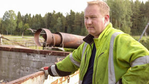 Skrothandlarn själv. Stefan Norrlin är huvudperson i syrrans dokumentär. Stefan Norrlin i gul jacka och med skrot i bakgrunden.