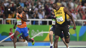 Usain Bolt i gult grinar sig över mållinjen.