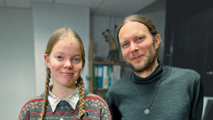 Tytär Kerttu Suominen ja isä Osma Suominen seisovat vierekkäin ja hymyleivät. Heillä on kummallakin kaulassaan Prometheus-leriltä eri vuosina saamansa korut.