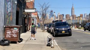 Gata i Brooklyn, NY Utsikten från Brooklyn mot Manhattans skyskrapor. Vårdag i värmen. Man i shorts passerar graffitiklottrad soptunna