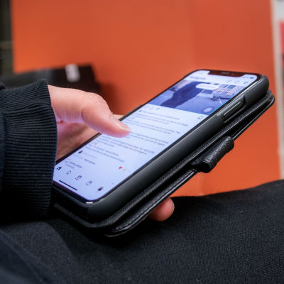 Hand håller i smarttelefon och scrollar med tummen på en sociala medier-app. 