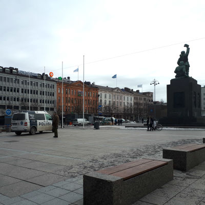 En ensam man står bredvid en polisbil på Vasa torg. Frihetsstatyn syns i bakgrunden.