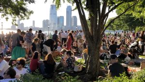 Hudson-floden och New Jersey ger bakgrund för picknicken. Trängsel i piknik-parken med utsikt över Hudson mot New Jersey.