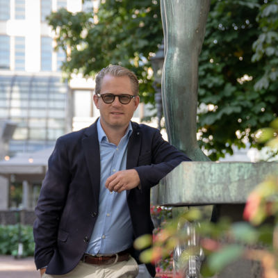 Joachim Thibblin står lutad mot en staty i Esplanadparken i Helsingfors.