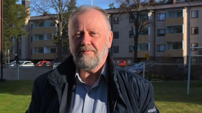 Man i blå jacka står på en höghusgård.