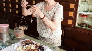 Traditionella kinesiska läkemedel används också i Malaysia. I Kina blir de allt mer populära. En kvinna lägger något torrt material i en liten vågskål och i andra handen håller hon en liten tyngd. På bordet finns olika sorter av torkat material och bakom henne finns en hylla med många små lådor och en del glasburkar.