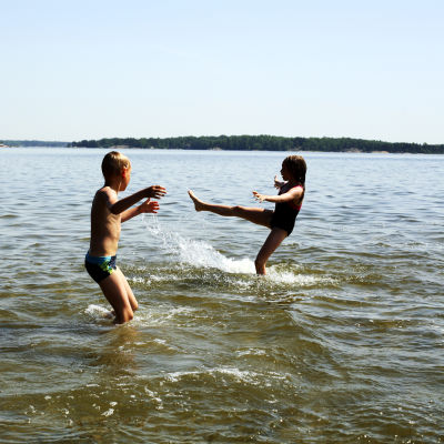 Två barn leker i vattnet under en varm sommardag.