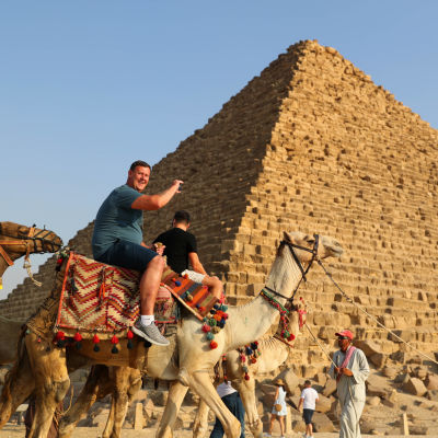 En turist rider på en kamel vid en pyramid i Egypten. 