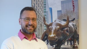 Tjuren symboliserar uppgång. En man står framför en tavla som är ett fotografi av en staty i brons föreställande en tjur. Det är en bild tagen vid Wall Street i New York.