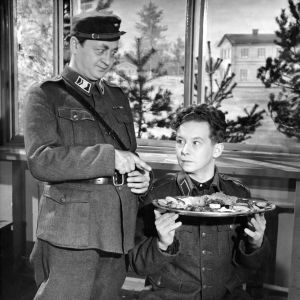 Ylivääpeli (Pentti Viljanen) yllättää ylellisen aterian tilanneen alokkaan (Lasse Pöysti).