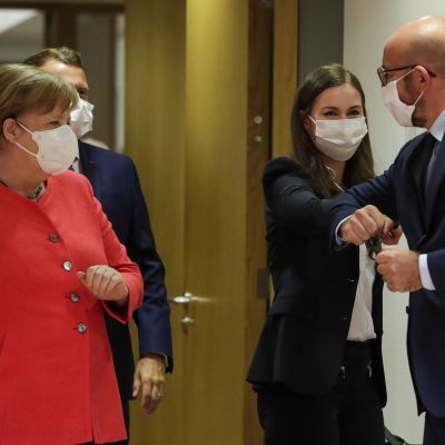 Sanna Marin armbågshälsar med Charles Michel. Tysklands förbundskansler Angela Merkel tittar på från sidan. Alla är iklädda munskydd.