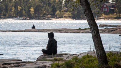En människa sitter vid stranden och ser ut över vattnet.
