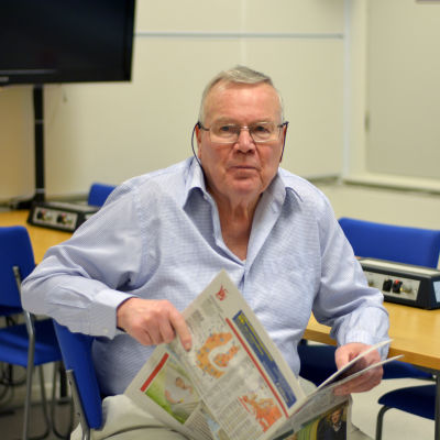 Ralf Friberg sitter med en tidning i handen.