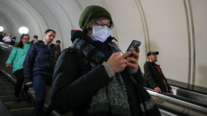Att använda munskydd är kanske inte den bästa idén i kampen mot coronaviruset. En kvinna med ansiktsskydd står i rulltrappor och knäpper på sin telefon.