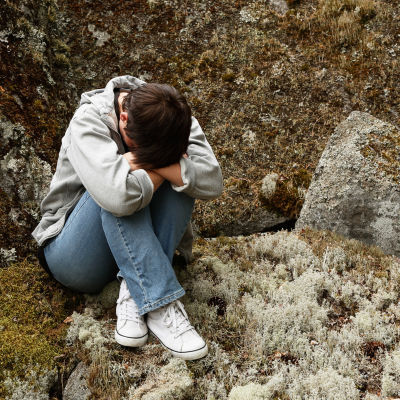 Ensam kvinna sitter på en sten i skogen.
