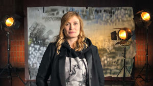 Miia Tervo seisoo studiossa taustalavasteen ja studiolamppujen edessä. Kuva otettu lyhytvideosarjaan Me elokuvantekijät.