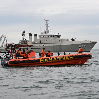 En gummibåt med räddningspersonal ombord och i bakgrunden ett fartyg från marinen.