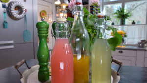 Kolme erilaista alkoholitonta vaihtoehtoa ruokajuomille lasipulloissa keittiössä.