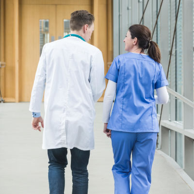 En sjukskötare och en läkare fotograferade bakifrån medan de går i en sjukhuskorridor.