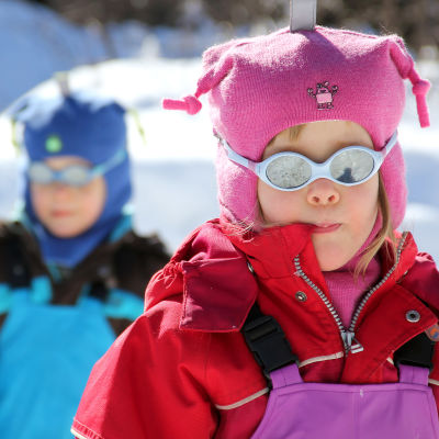Två barn i treårsålder, ute i snön med polariserande solglasögan. 