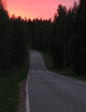 aurinko laskee, tie kiemurtelee metsässä