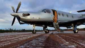 Det första flygplanet som landade på flygplatsen i Pyttis. Flygturerna började den 16 november 2017. Ett silverfärgat litet passagerarflygplan står på en landningsbana av jord. Det ligger frost på marken.