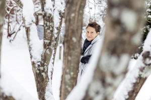 Heini Hirvonen ulkona, katsoo kameraan puitten runkojen välistä.