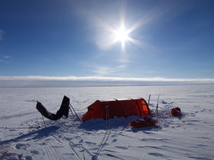 Att slå upp tält varje dag. Vardagsliv med en twist. Ett orange tält. Runt omkring finns bara is och snö. Solen lyser.